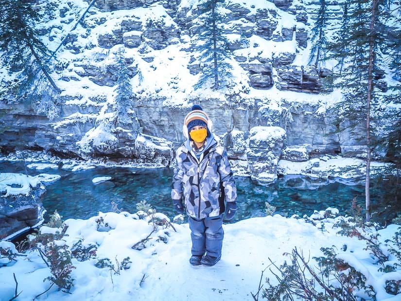 A kid standing beside Maligne River in winter
