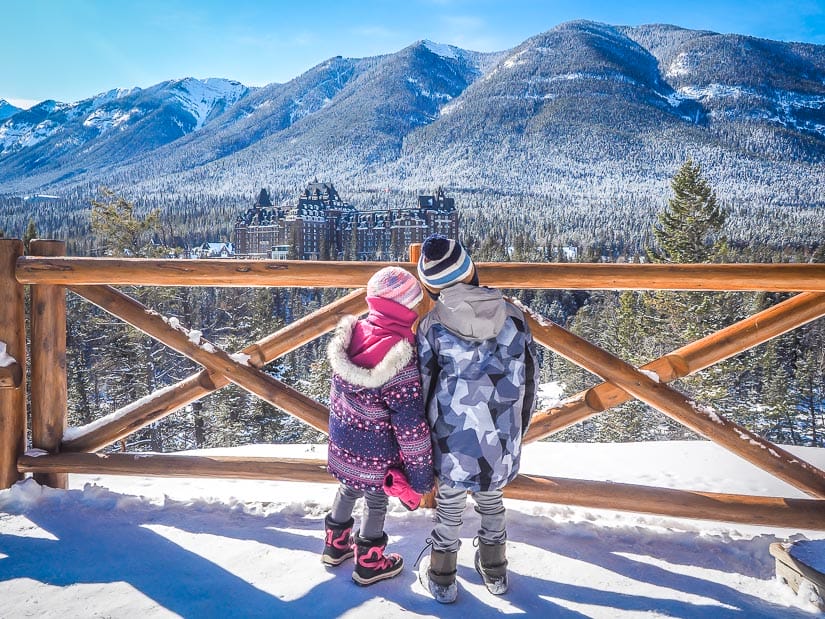 Two kids standing at Surprise Corner and looking at the view of Banff Springs Hotel in winter