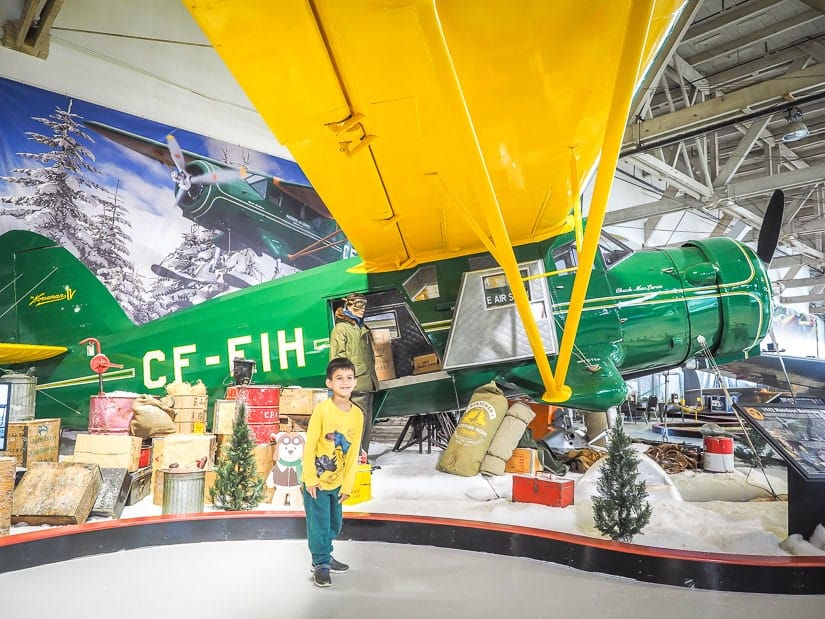 A kid standing in front of an old airplane display at Alberta Aviation Museum