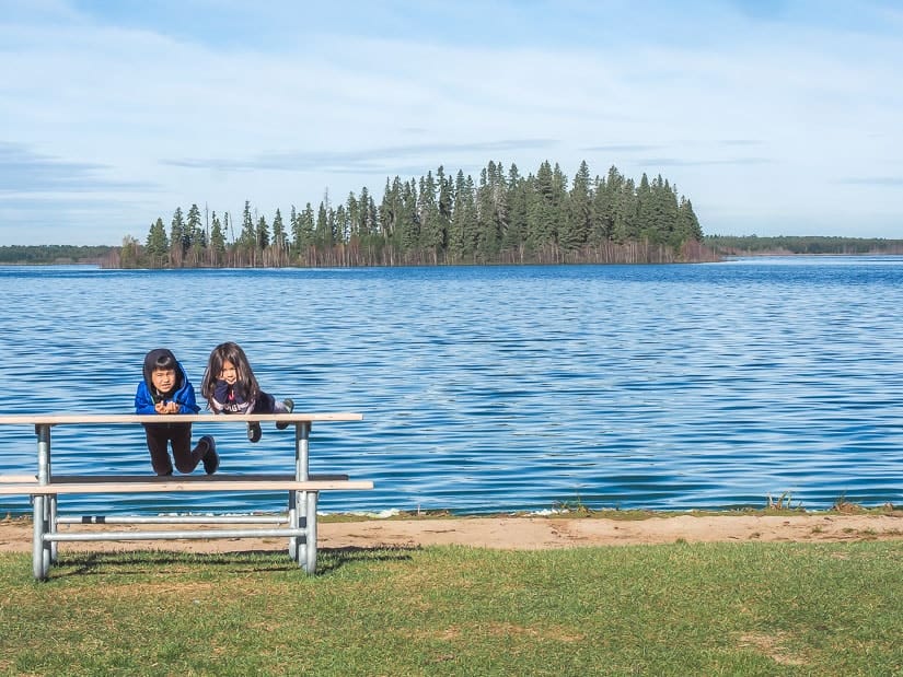 Two kids on a picnic table with Astotin Lake in the background