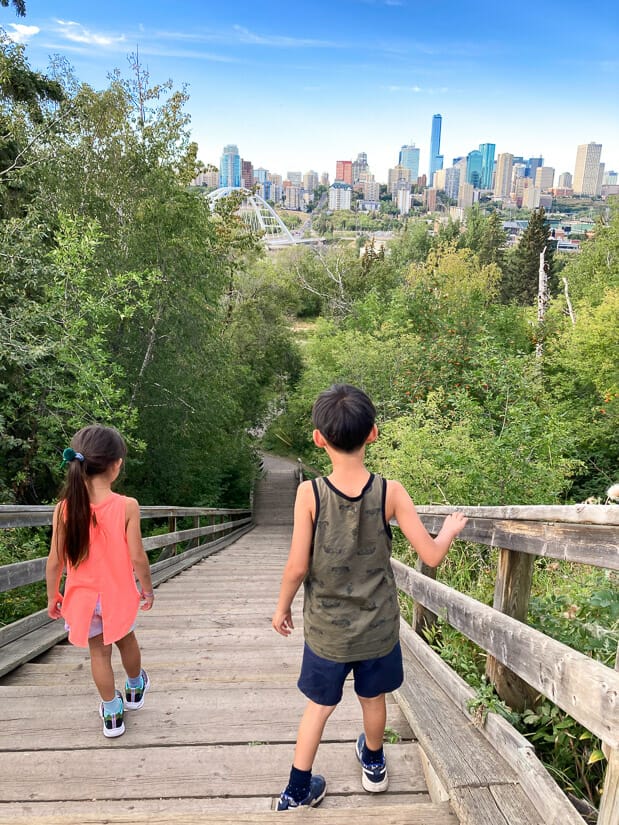 Two kids hiking in the Edmonton River Valley with downtown Edmonton visible in the distance