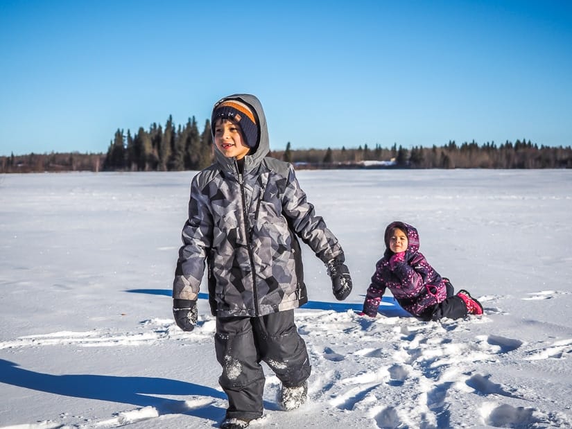 Two kids playing in the snow on a frozen lake in Elk Island National Park
