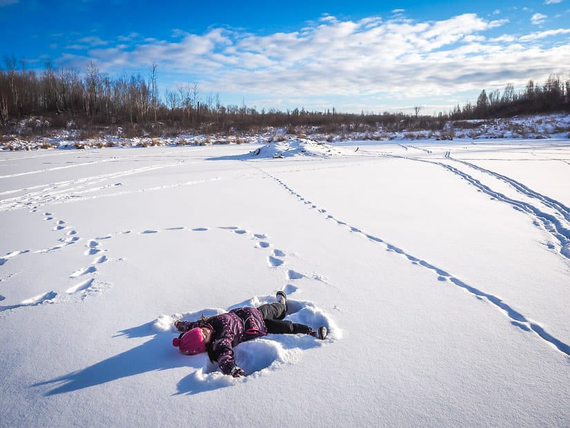 A kid doing a snow angel on a frozen pond in Elk Island National Park