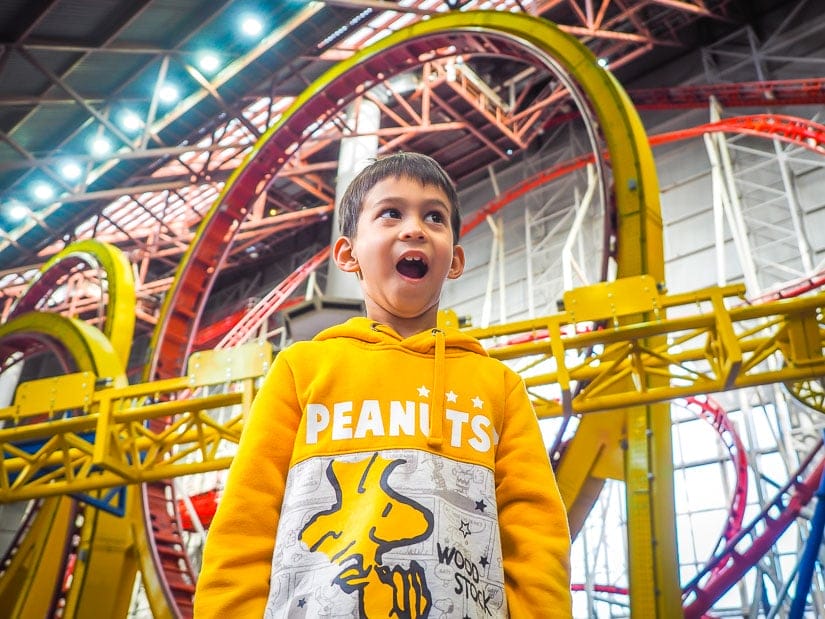A kid looking excited as he stands in front of a huge indoor rollercoaster in Galaxyland, West Edmonton Mall
