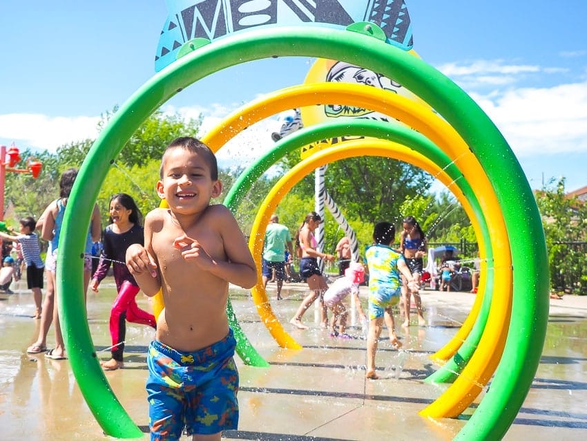A boy running through a row of sprinklers at Jackie Parker Spray Park in Edmonton
