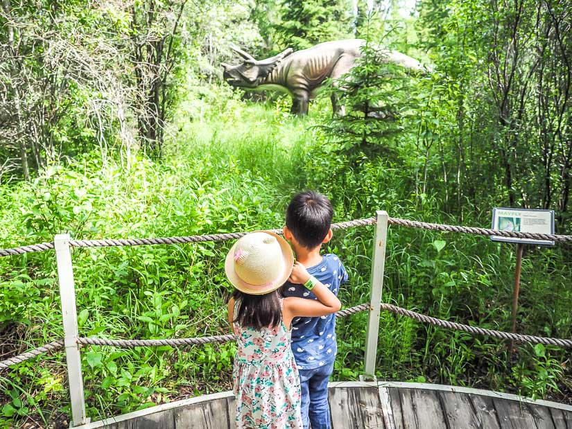 Two kids looking at a dinosaur statue in Jurassic Forest, a good Edmonton day trip with kids