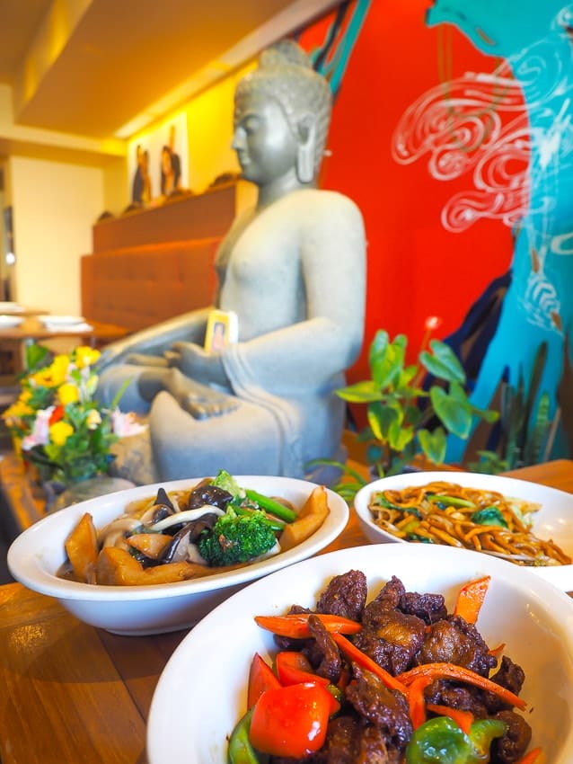 Vegan dishes on a table with a Buddha statue in the background at Padmanadi, Edmonton's best restaurant