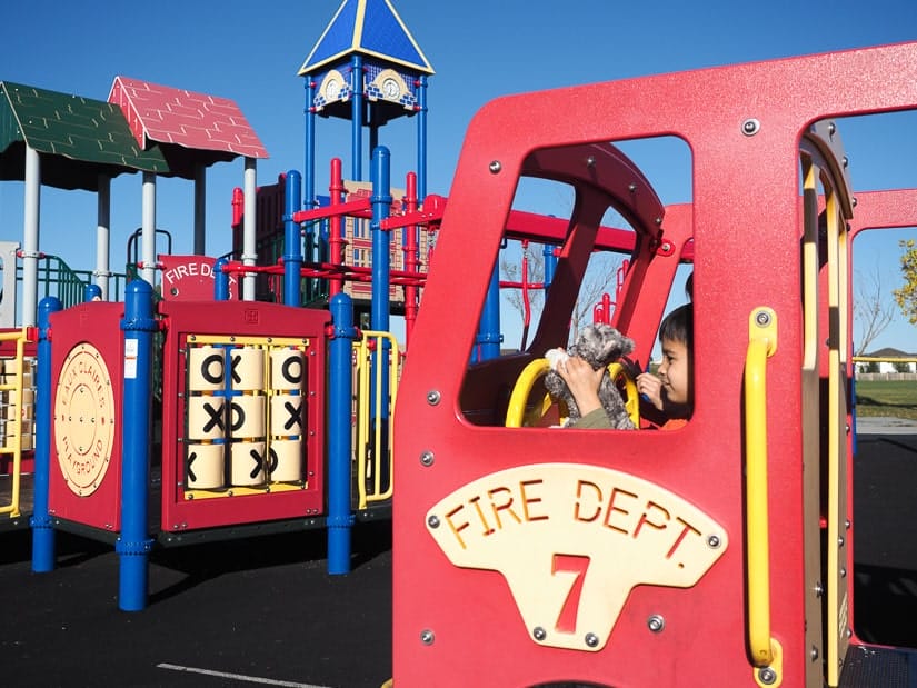 A kid pretending to ride a fire engine in Eaux Claires Playground in Edmonton