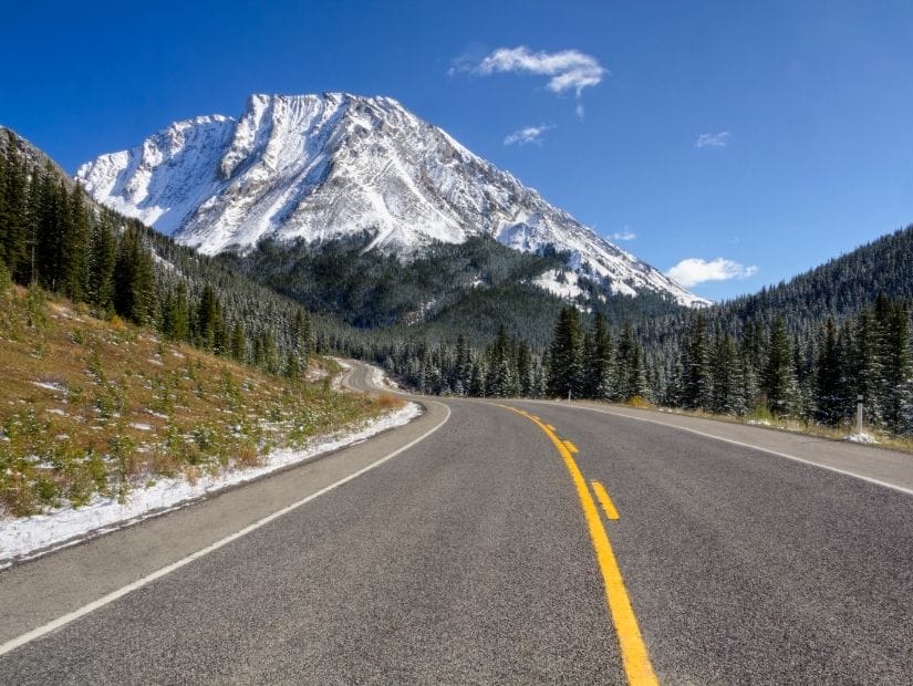 The road of Highwood Pass, with a snow covered mountain in the background