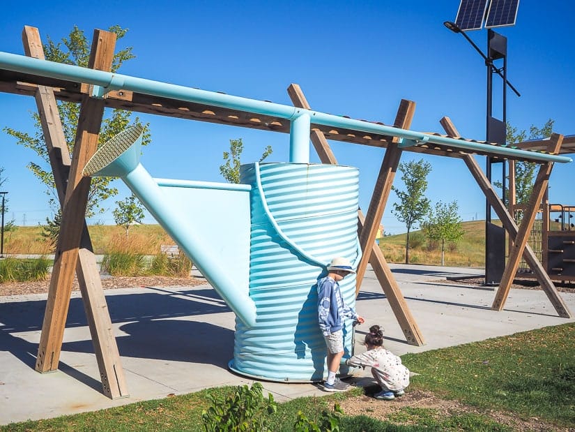Two kids getting water from a giant watering can at The Hills in Charlesworth Sustainable Park.