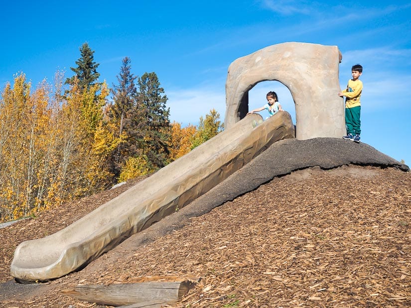 Two kids playing on Cement slide at Spruce Grove Natural Playground