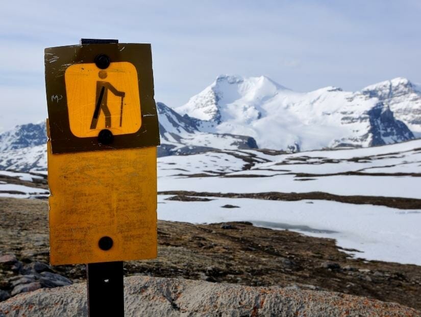 A hiking sign with snowy mountains in the background