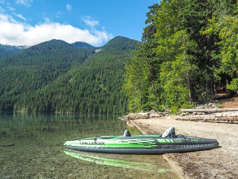 A green kayak on the shore of a mountain lake with very clear water