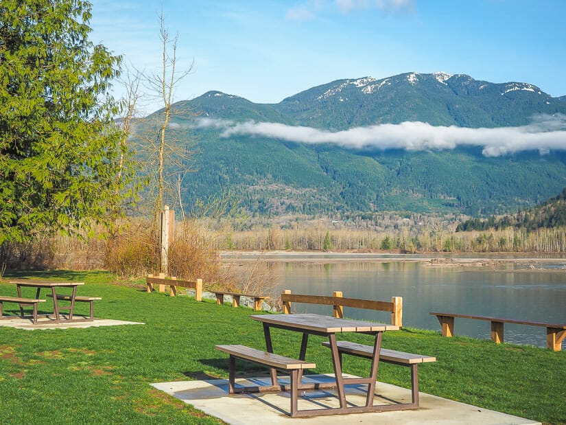 Picnic tables beside the river and mountains across the river at Island 22 Regional Park, Chilliwack