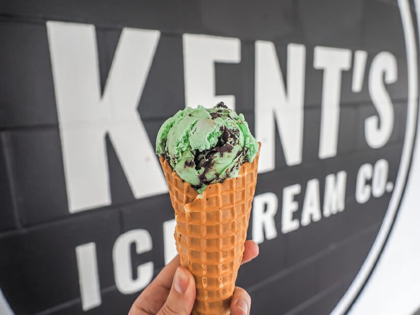 A waffle cone with chocolate mint ice cream in front of a sign for Kent's Ice Cream in Chilliwack