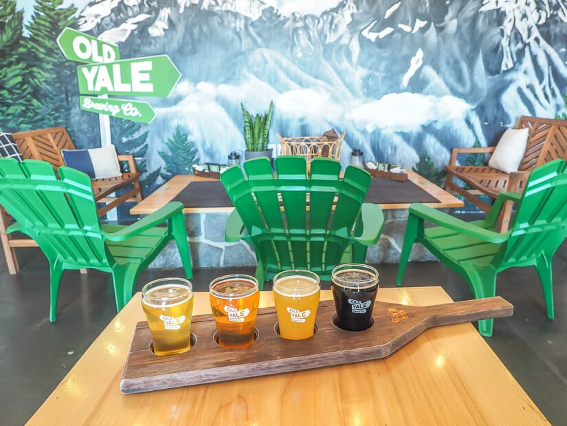 A flight of beers on a wooden table with green chairs and mountain mural on the wall behind it at Old Yale Brewing, Chilliwack