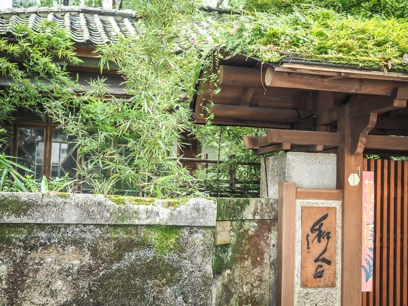 A tradition wooden gate with a Japanese teahouse and trees behind it