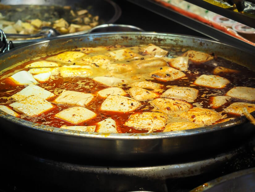 A huge wok filled with blocks of tofu simmering in spicy soup