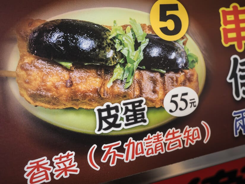 A food vendor menu sign that shows stinky tofu with 100-year egg and a price of 55NT on it