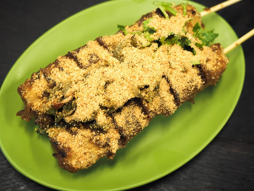 Two logs of stinky tofu topped with greens and peanut powder on a green plate