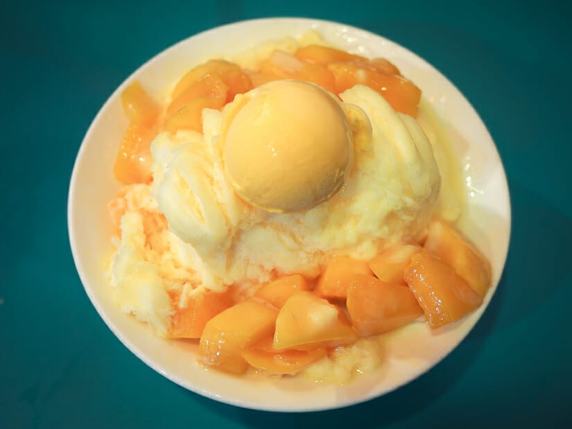 A bowl of mango shaved ice with a scoop of orange mango ice cream on top