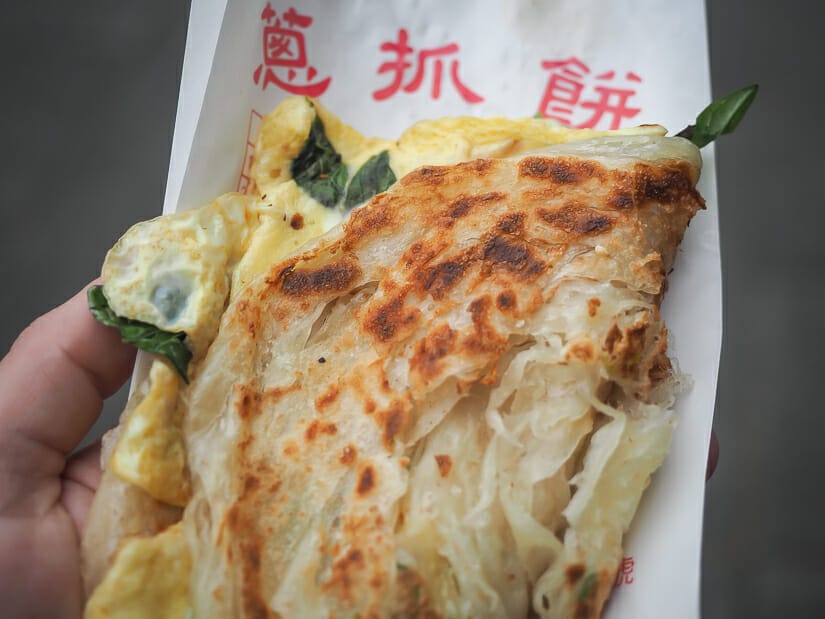 Close up of a green onion cake folded in half on a paper bag that says "green onion cake" in Mandarin.