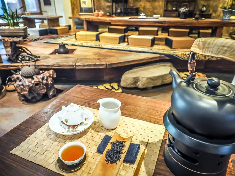 A pot of tea and various tea brewing equipment on a wooden table, with traditional wooden low tables in the background in a teahouse on Yongkang Jie