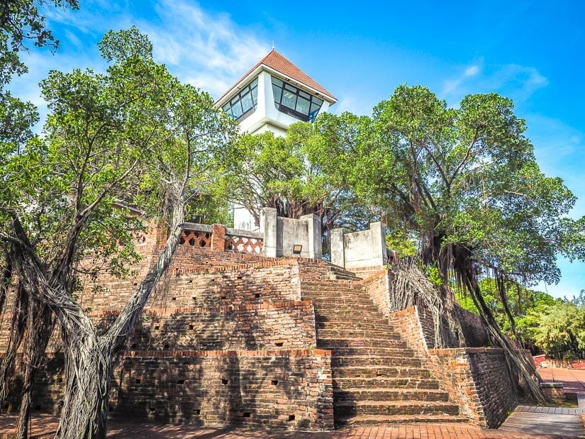 Steps going out the ruins of a fort, with trees growing on a the fort, and a white watchtower at the top