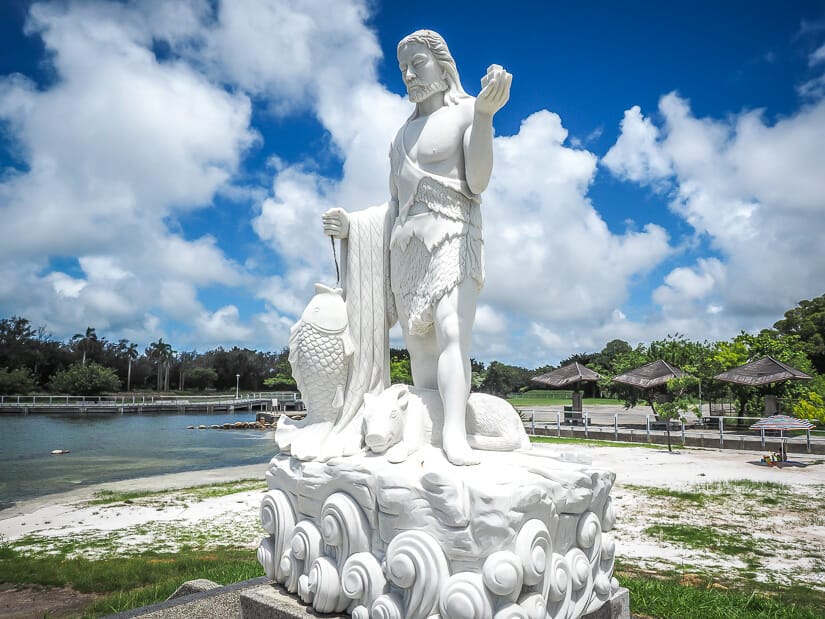 A white statue of a god holding a fish white white beach and blue sky behind it
