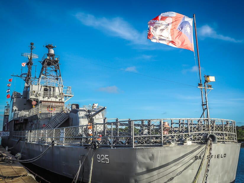 A huge war ship parked in Tainan Harbor with an ROC flag with a cute dog flying at the front