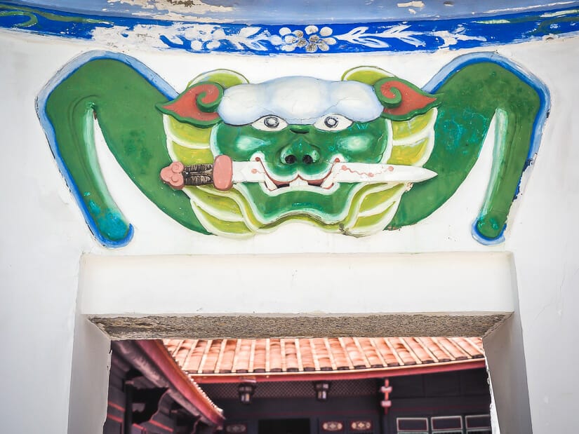 Symbol of a green lion with a sword in its mouth on a white wall at the entrance to an old house in Anping, Tainan