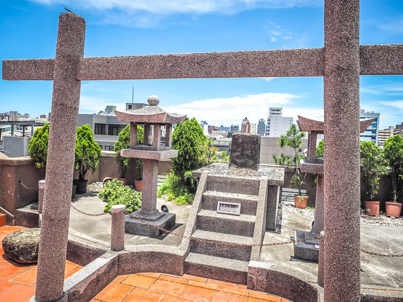 A Japanese stone gate and other ruins on a red rooftop with other buildings in the background