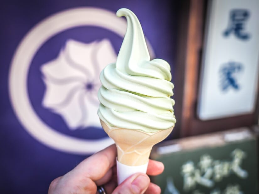 A hand holding a soft serve ice cream cone with purple sign and Chinese characters in background