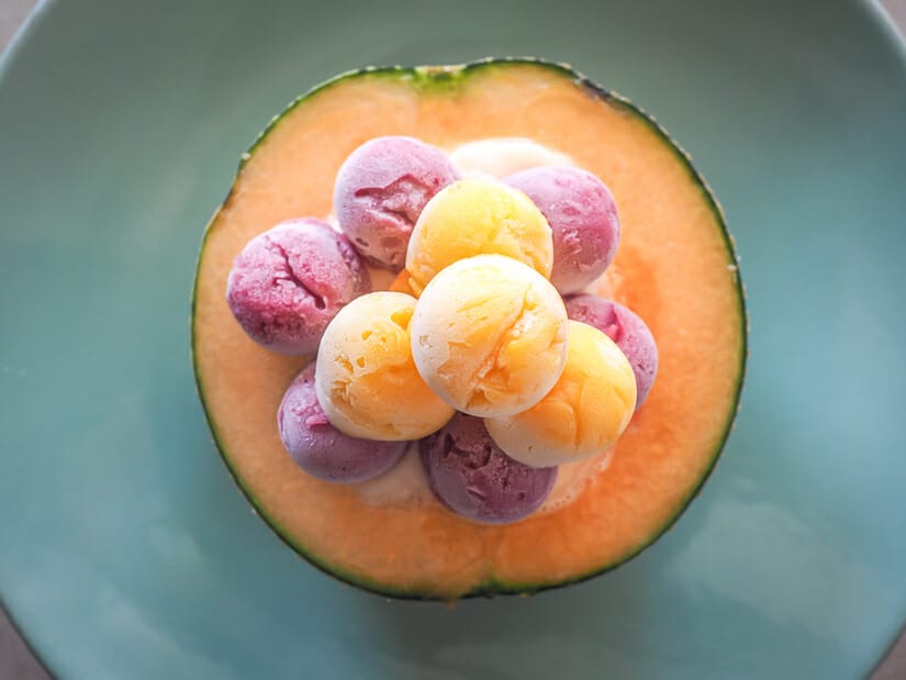 A half a cantaloupe on a plate filled with scoops of ice cream