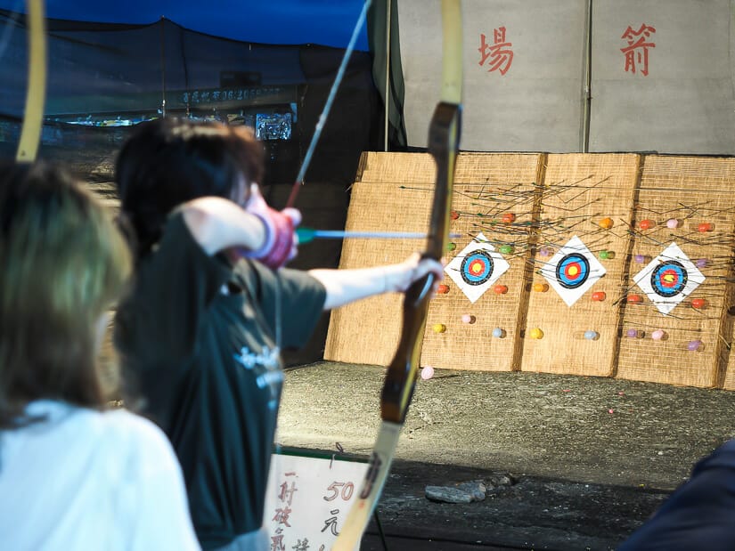 A girl shooting a bow and arrow at a target and some balloons at Wusheng Night Market
