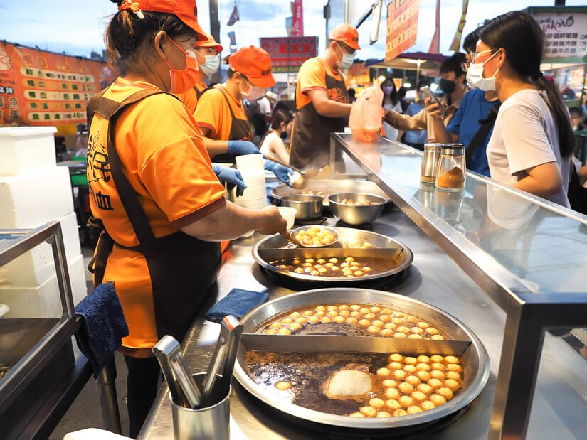 A food vendor standing over a pot of fish balls in duck blood and talking to the customer at Ta-Tung Night Market