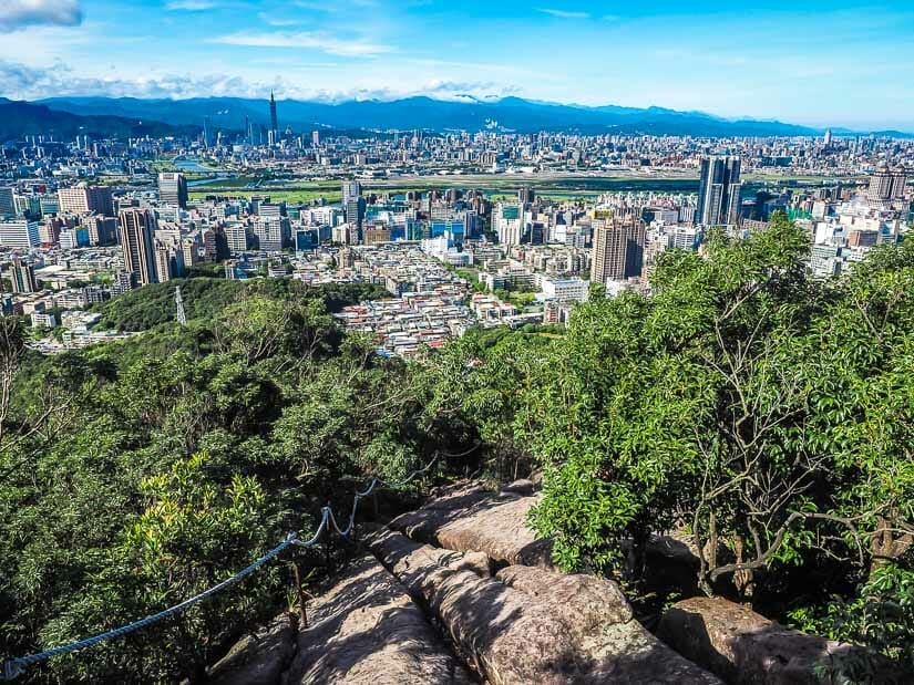 A rocky hiking trail in the foreground, with view of Taipei City in the background