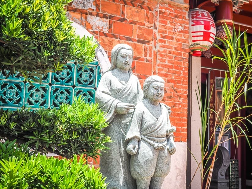 Stone statue of a boy and his mother in front of a red brick temple, the Koxinga Ancestral Shrine