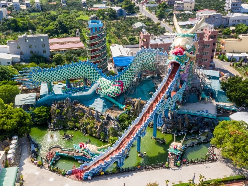 Aerial/drone view looking down on a large Taiwanese temple complex, including a tall red and blue staircase leading up into a huge dragon's mouth