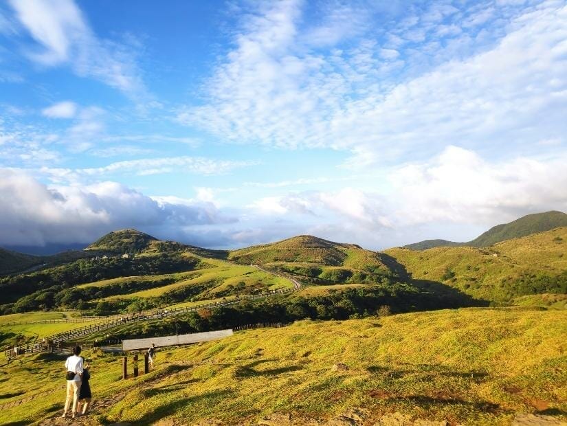 A mountaintop grassland hiking trail in Yangmingshan with two people walking on the trail