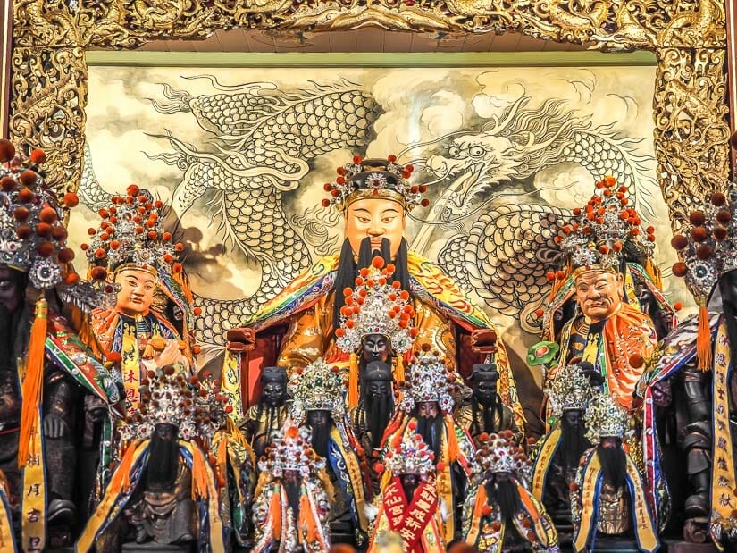 Statues of gods on an altar with a dragon painting behind them