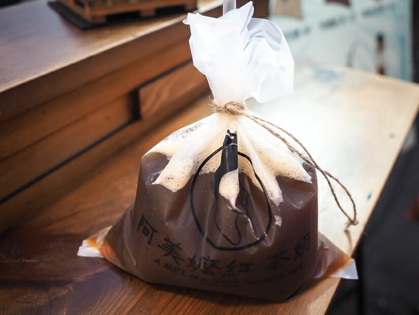 A plastic bag of brown iced tea with a straw in it on a counter of a food stall at Dadong Night Market