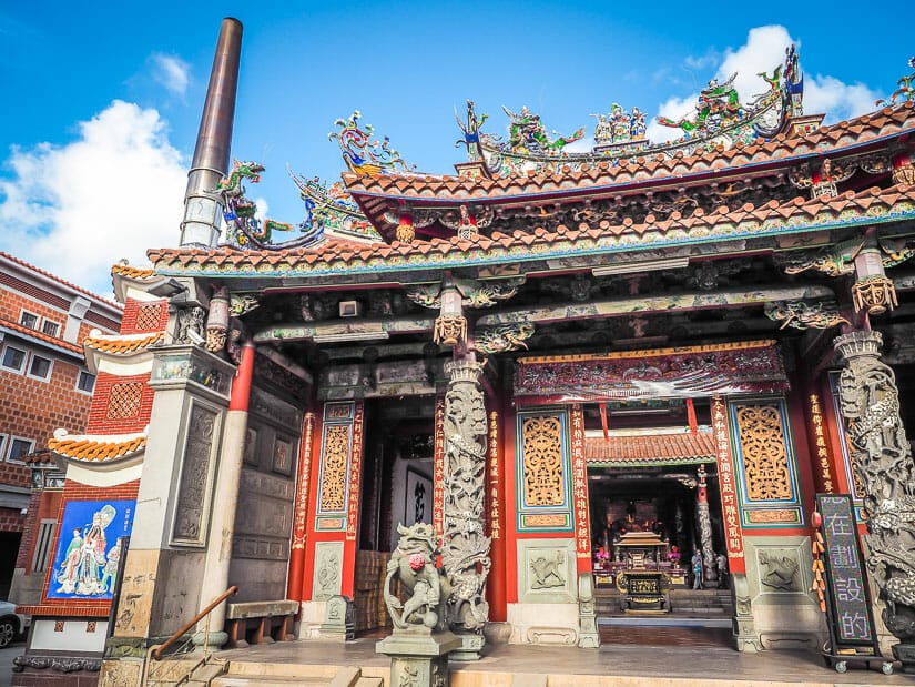 Exterior of the front of the Tainan Grand Matsu Temple, including entrance, stone lions, and a tall smokestack for burning ghost money