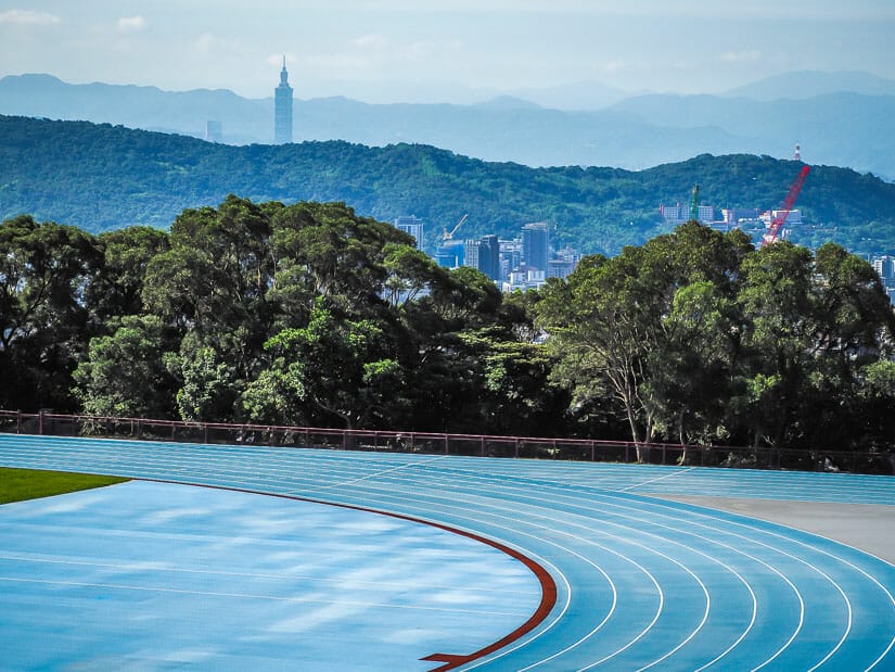 A blue running track in the foreground, with Taipei 101 poking out in the background