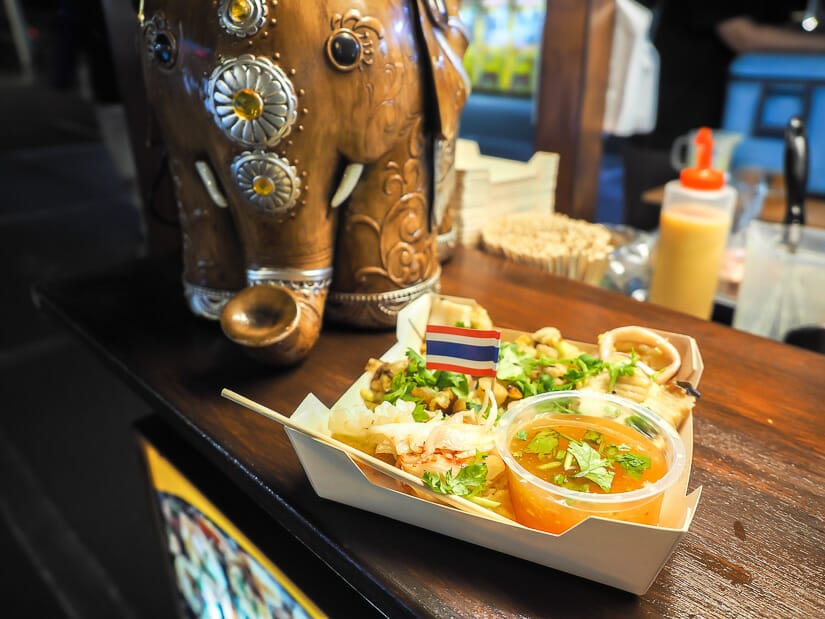 A night market stall with a dish of seafood cakes with a little Thai flag in it and an elephant statue beside it