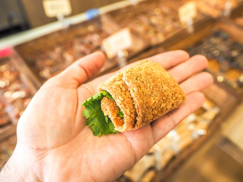 A hand holding a roll of soft peanut brittle wrapped around cilantro