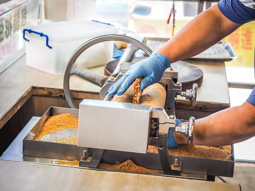 A hand putting peanut brittle into a press machine in Anping