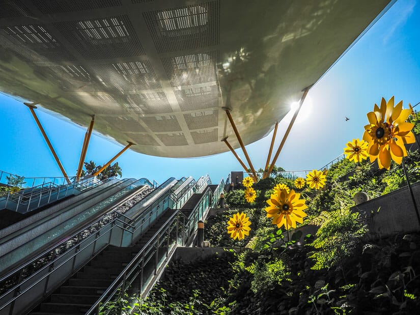 An MRT exit into Kaohsiung's Central Park, with escalators going up and some spinning yellow flower decorations