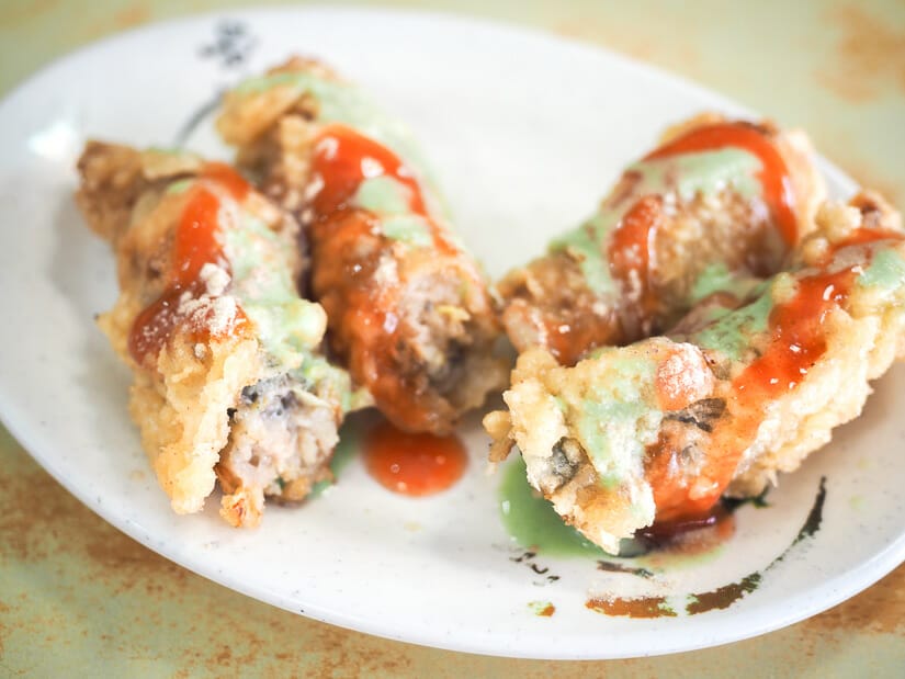 A plate of deep fried oyster rolls with wasabi and spicy sauce on them