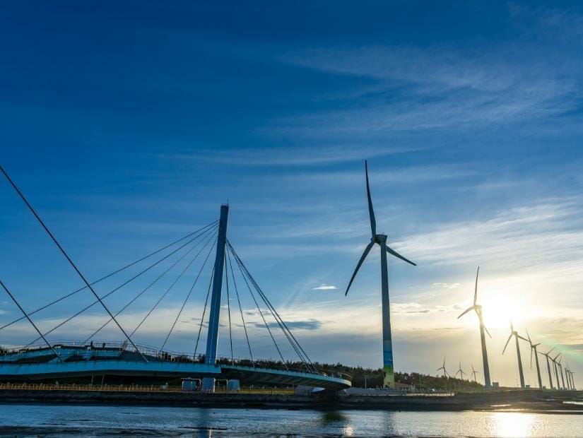 A bridge filled with pedestrians and row of wind turbines at Gaomei Wetland